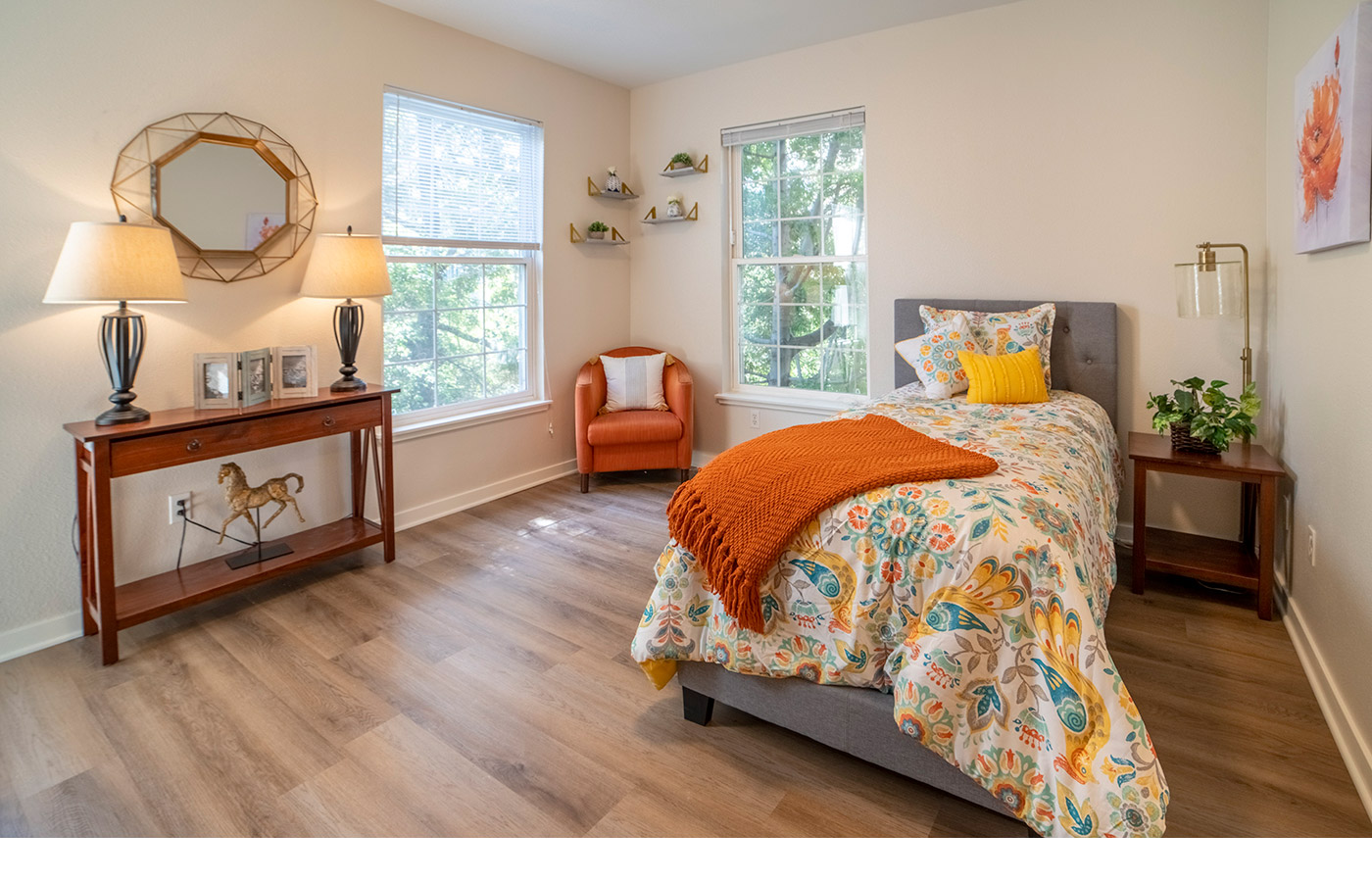 Furnished bedroom with a bed, dresser, and large windows.