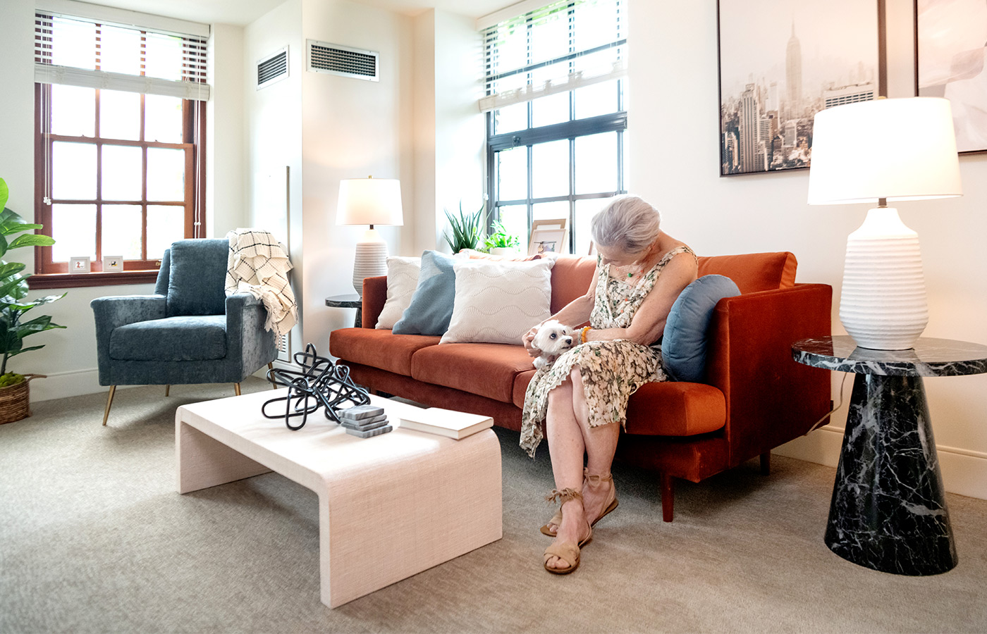 A resident in their furnished living room space with sofa, table, and seating area.
