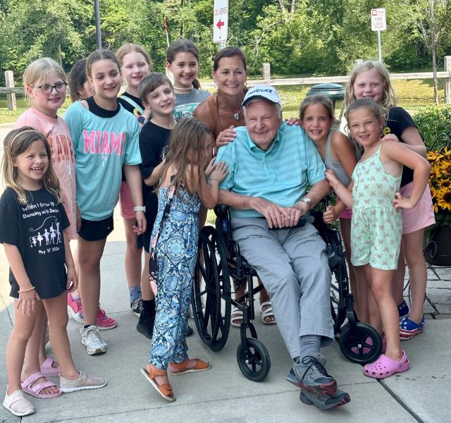 A group of kids around resident in wheelchair.