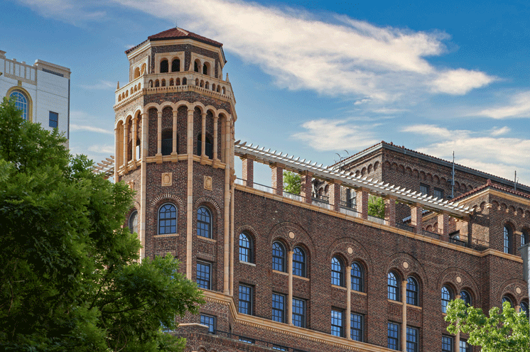 One of the original tower structures displayed against a blue and white sky with a vibrant green tree in front.