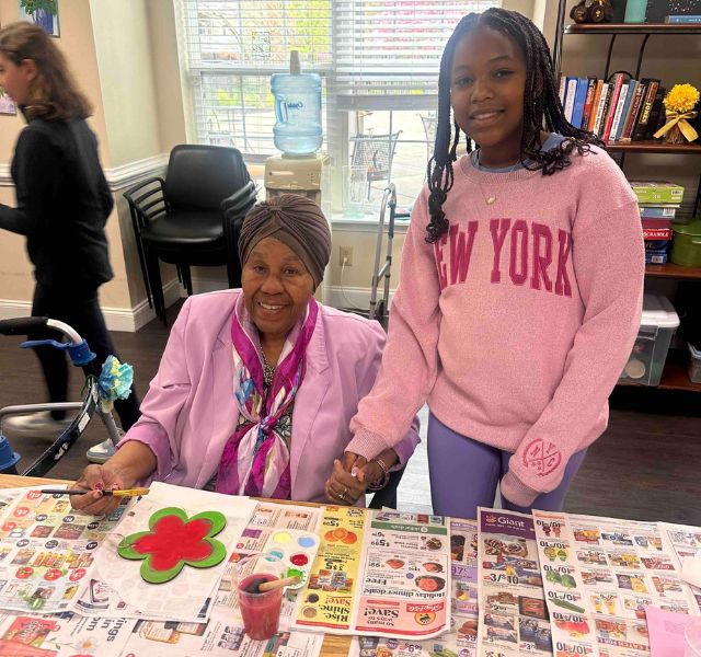 A resident painting and a young person standing next to the resident.