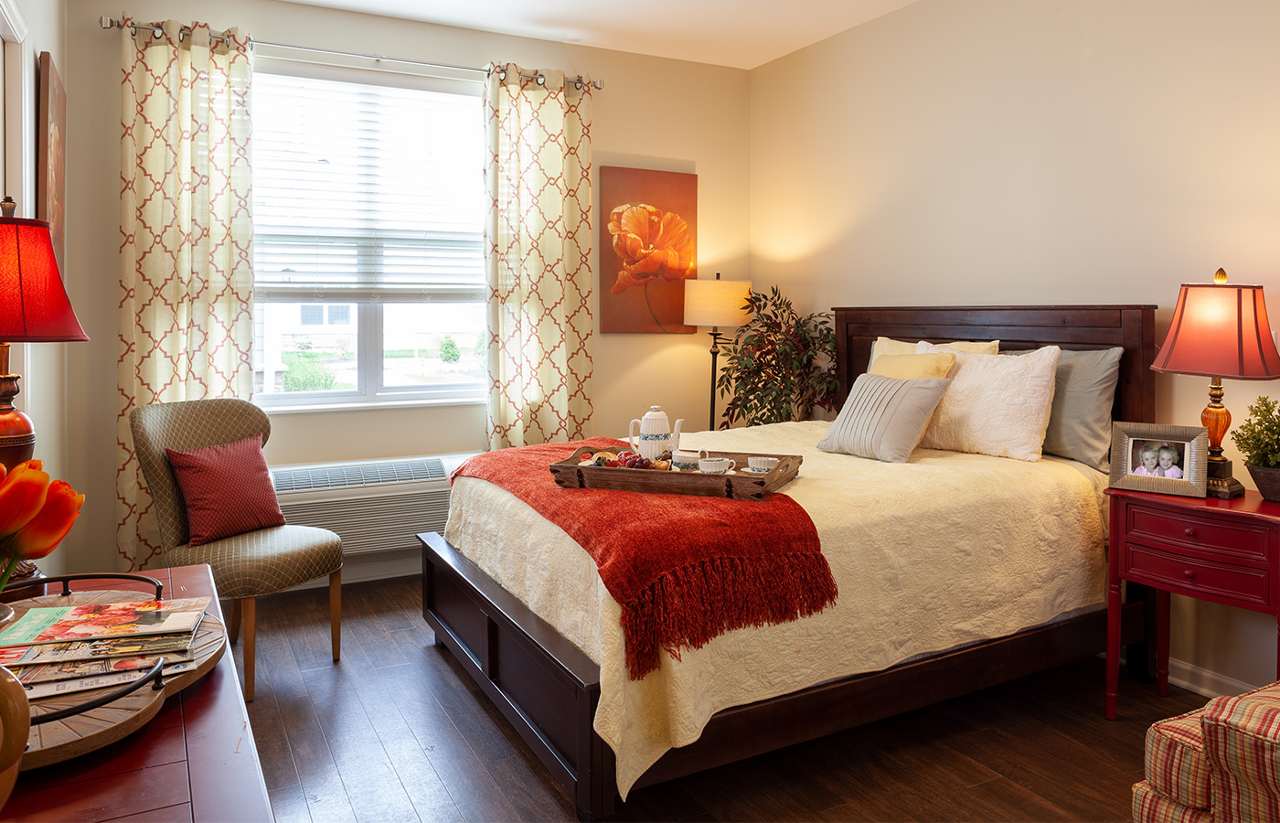 Furnished bedroom with tables, lamps, dresser, and window.