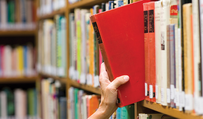 person taking a book from a shelf in a library