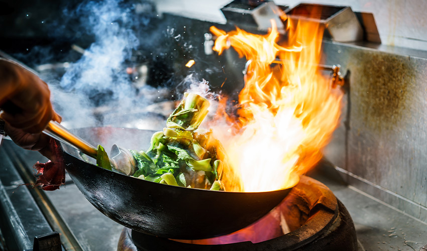 A wok on the stovetop with fire.