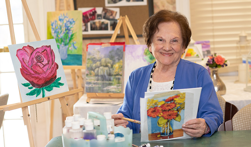 Resident Rosaria smiling with her artwork displayed around her